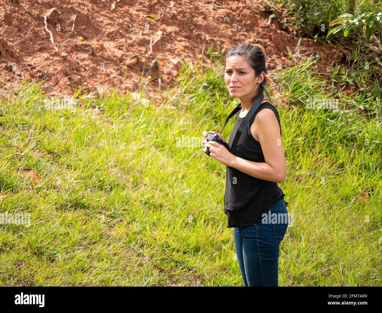 Young Short Hispanic Woman in Blue Jeans and Black Shirt Takes Picture with Compact Mirrorless Camera Stock Photo