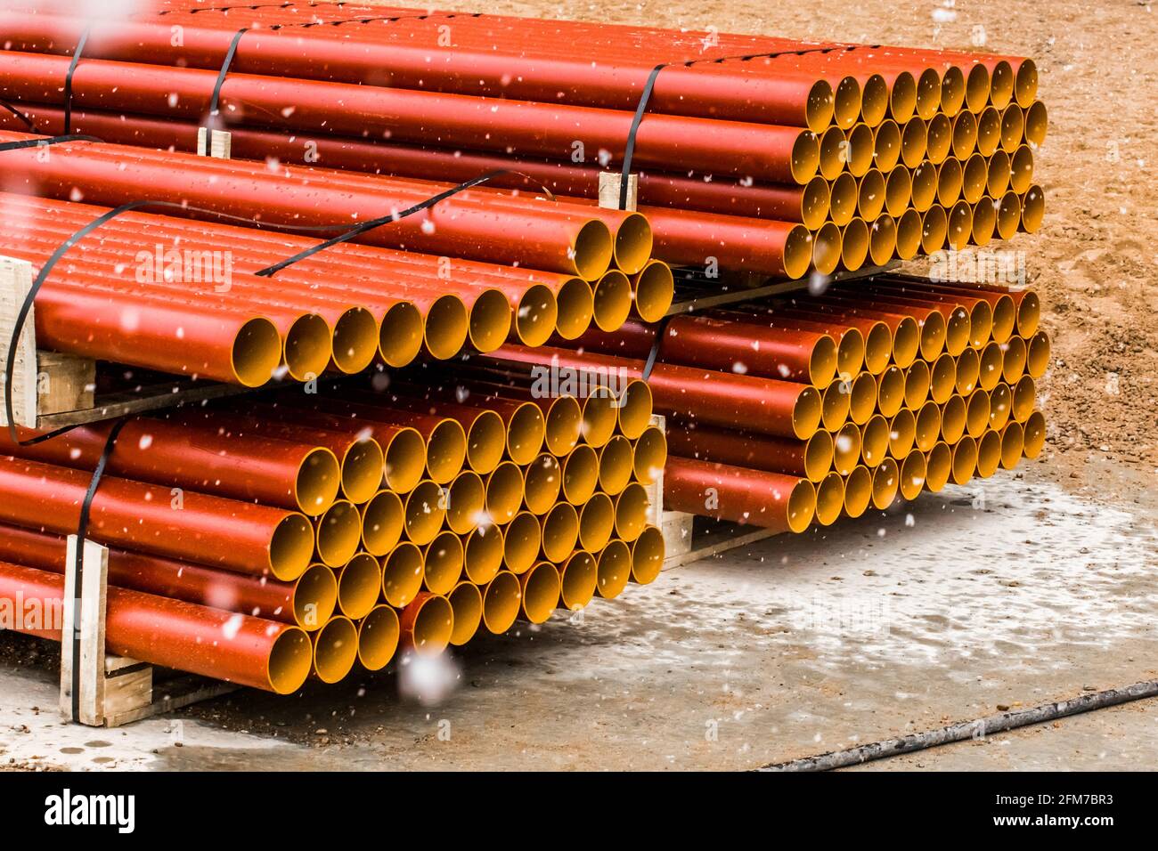 Pile of round industrial polyethylene thermoplastic pipes storage outdoor on a construction site with snow in cold winter. Stock Photo