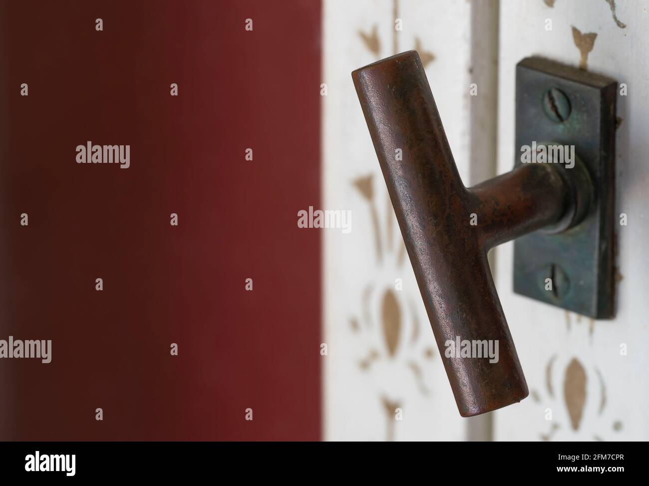 Background image of metal handle of an old white window and a part of the facade in burgundy red Stock Photo