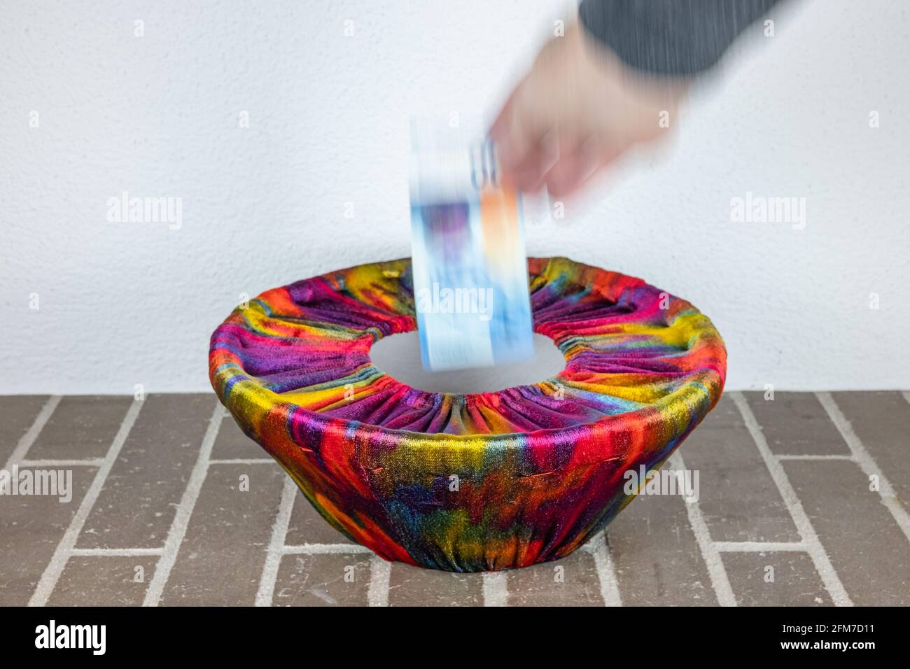 A human hand drops a swiss banknote into a basket dressed in colorful fabric Stock Photo