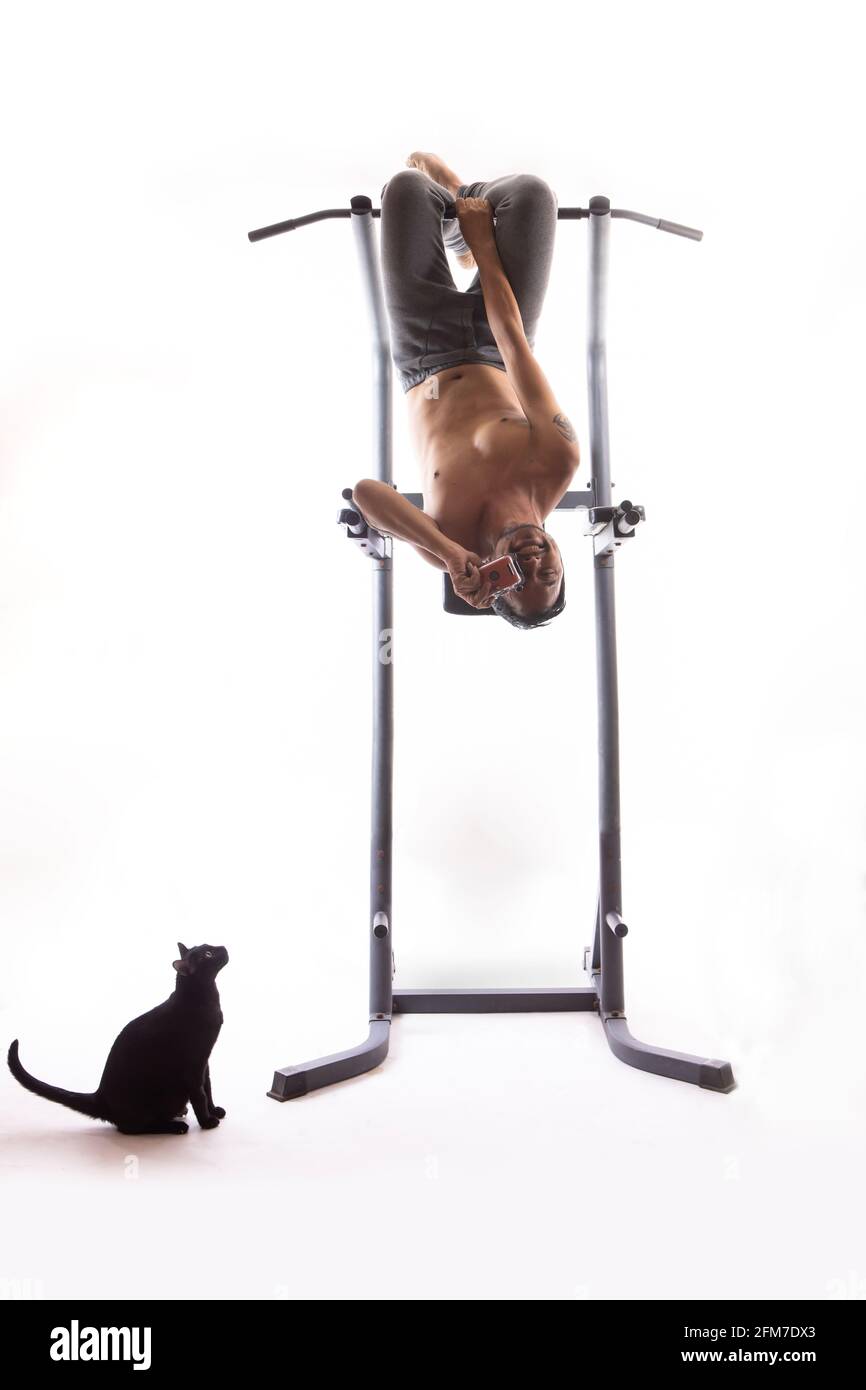 A man holds the camera upside down on an exercise machine, isolated on a white background.A black cat sitting looking at a man Stock Photo
