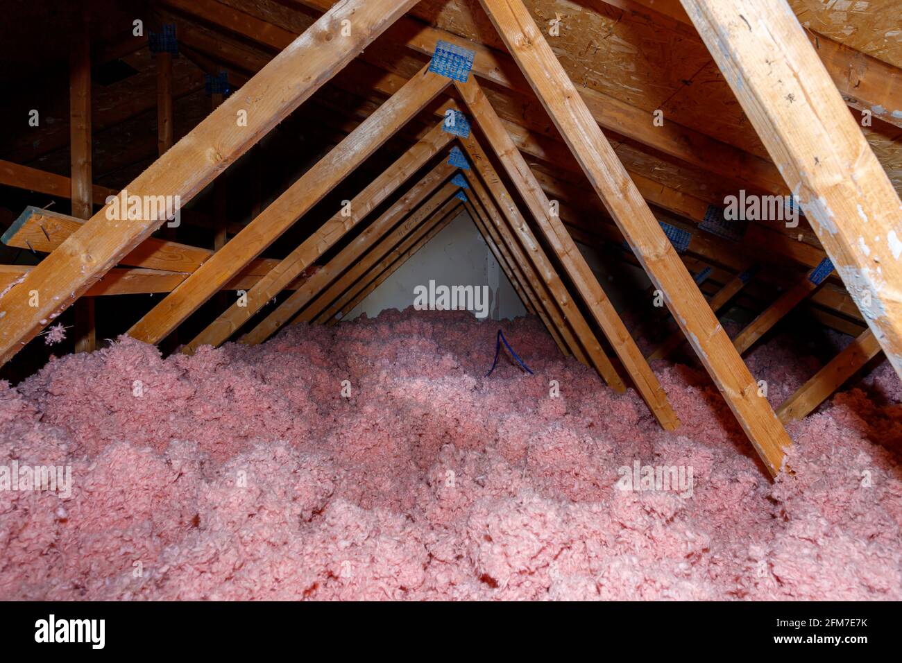 A dark attic in a woodframe house has pink loose fill fiberglass