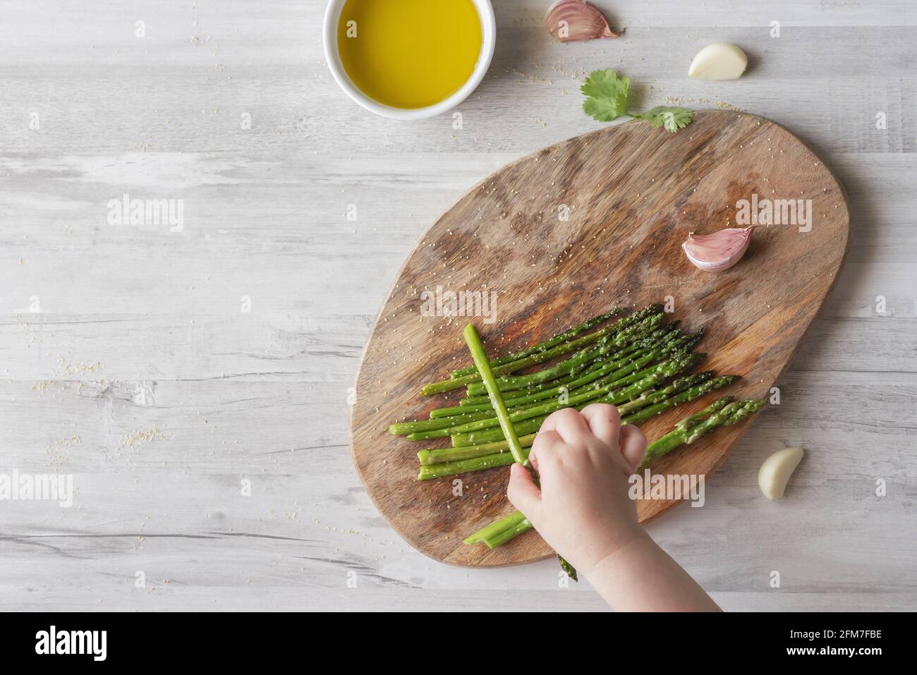 Top view of a woman's hand arranging green asparaguses on a wooden board in the kitchen Stock Photo