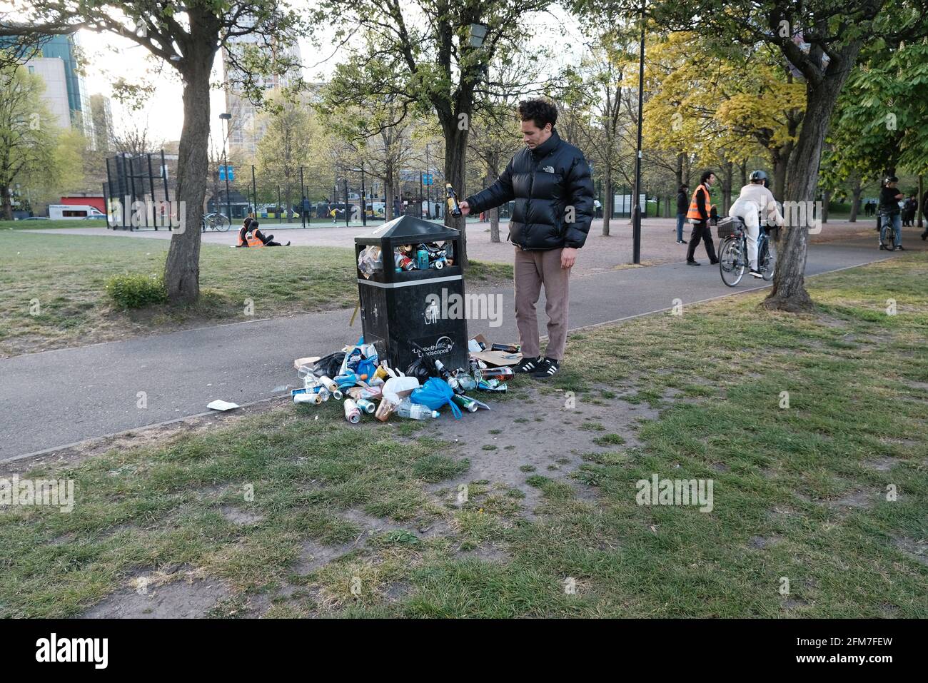 A man places an empty bottle in an already full bin in a park. People flock to outdoor spaces until indoor socialising is permitted once more Stock Photo