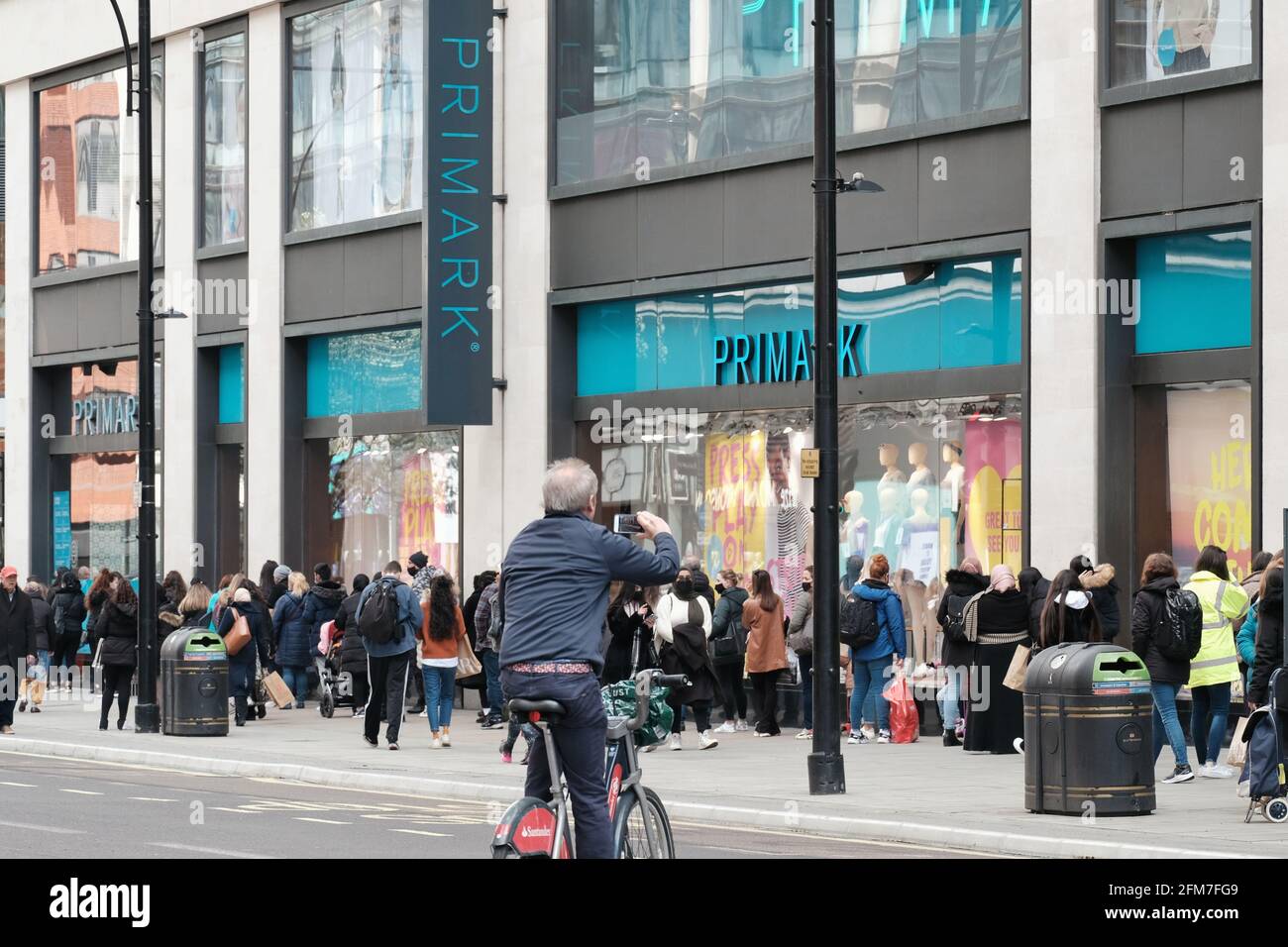 A man on a bicycle takes a photo of the queue outside a Primark store on the first day non-essential stores reopened as part of lockdown easing Stock Photo