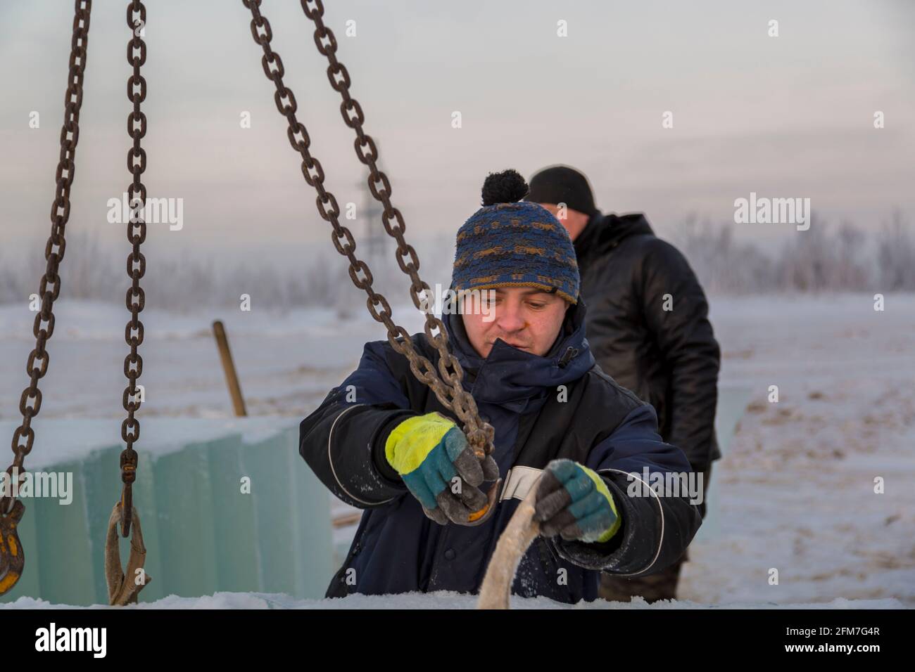 Portrait of a worker slinger in a blue jacket unloading ice blocks using a chain spider Stock Photo