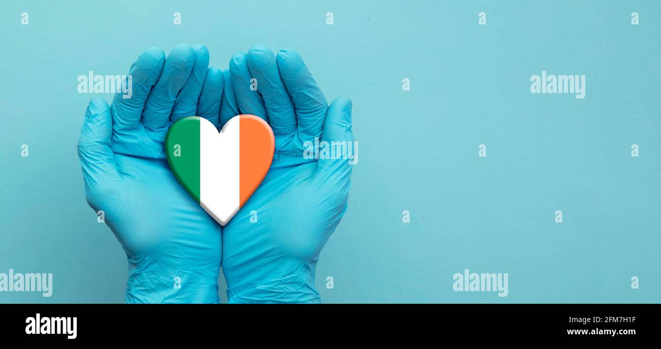 Doctors hands wearing surgical gloves holding Ireland flag heart Stock Photo