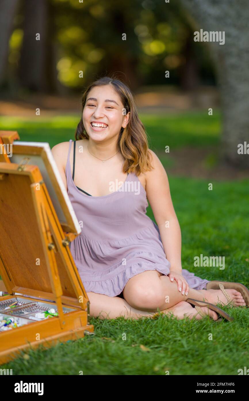 Petite Young Asian Woman Student Painting in the Park Using a Cabinet Easel Stock Photo