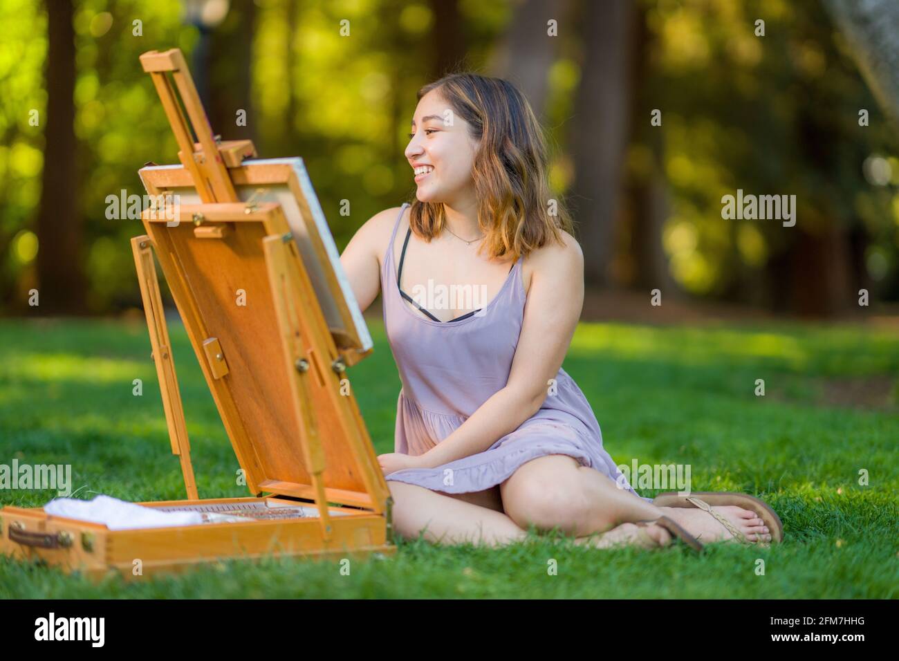 Petite Young Asian Woman Student Painting in the Park Using a Cabinet Easel Stock Photo