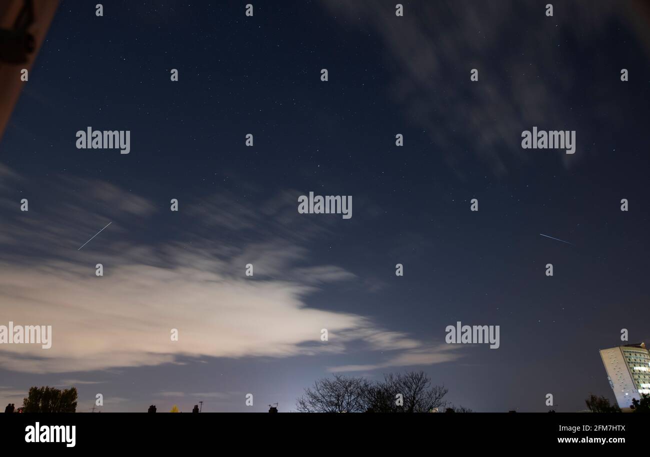 Wimbledon, London, UK. 7 May 2021. The Aquarids meteor shower hunt is called off in south west London as increasing cloud in the early hours of the morning builds up. The International Space Station makes a bright pass over London at 02.35am, seen to left in this image. The trail on the right (above high building) is from Meteor 1-29 satellite, an old weather observation satellite launched by the then USSR in the late 1970s. Credit: Malcolm Park/Alamy Live News. Stock Photo