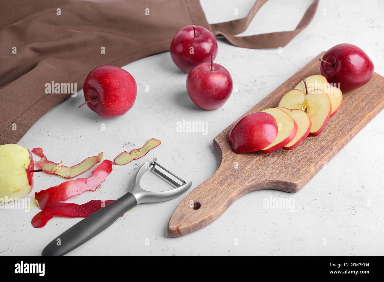 Board with cut red apples and peeler on table Stock Photo