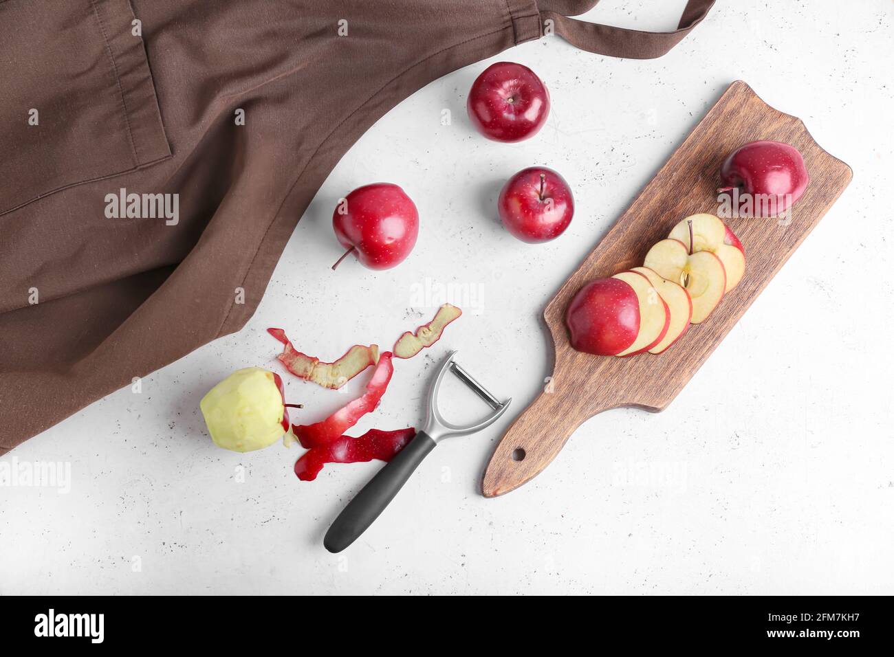 Board with cut red apples and peeler on table Stock Photo