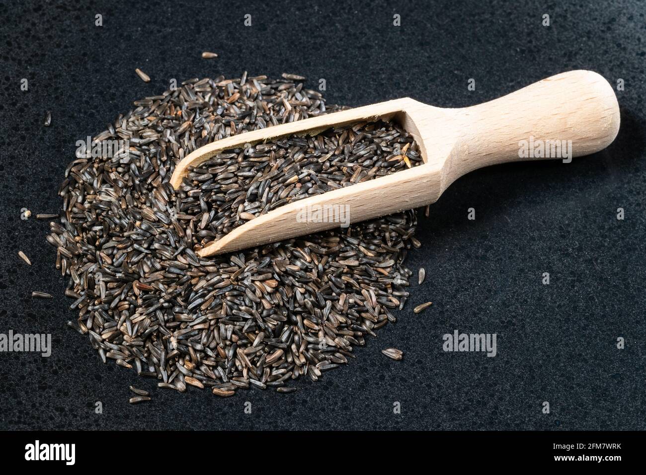 wooden scoop on pile of niger seeds (Guizotia Abyssinica) on black plate Stock Photo