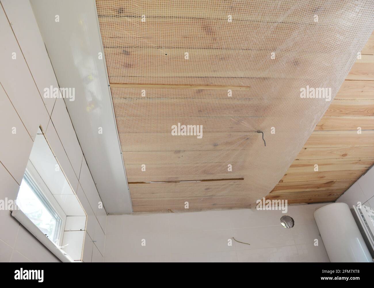 Bathroom renovation: Installing PVC ceiling cladding, plastic ceiling panels over a vapor barrier membrane and planked wood ceiling in a bathroom. Stock Photo