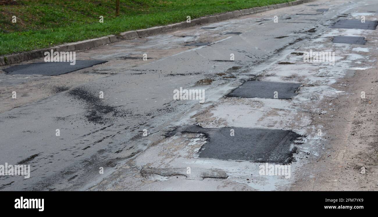 Asphalt road repair of poor quality. Pothole asphalt road repairs. A newly patched roadway in a bad condition. Stock Photo