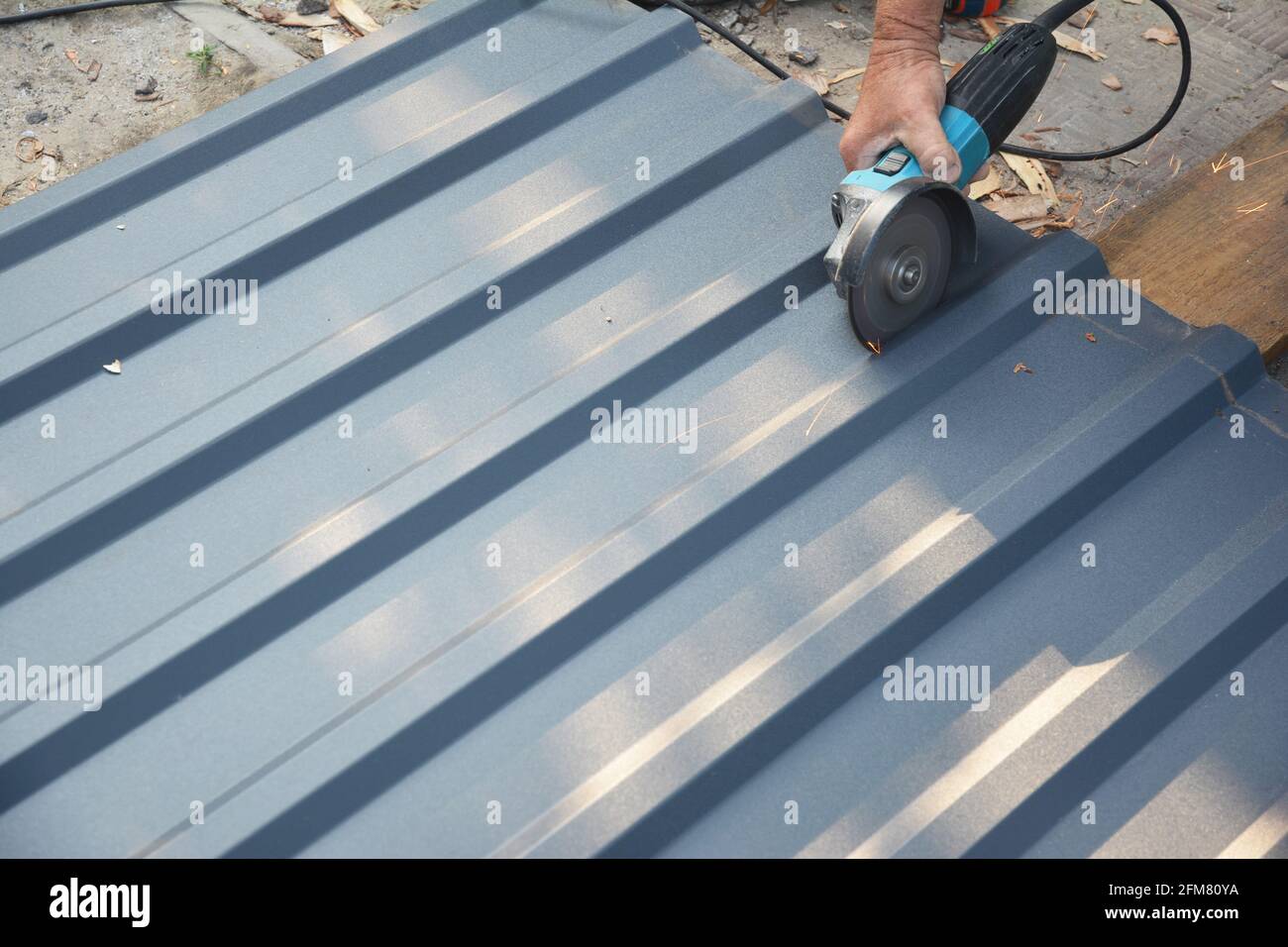 A roofer is cutting with a power angle grinder a corrugated metal roofing sheet, a metal roof tile. Stock Photo