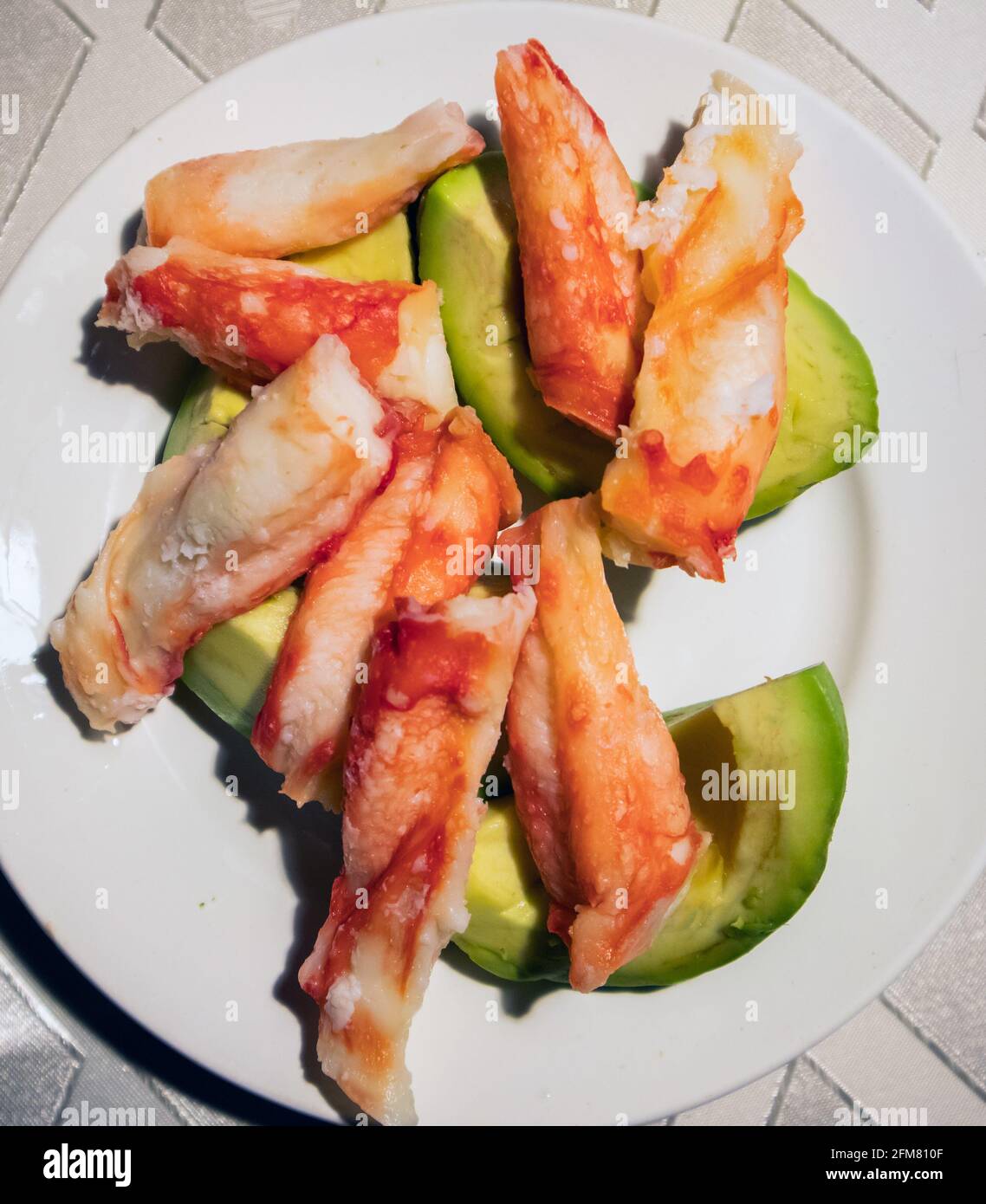 Peeled and cooked crab legs lying on a white plate with sliced ripe avocado Stock Photo