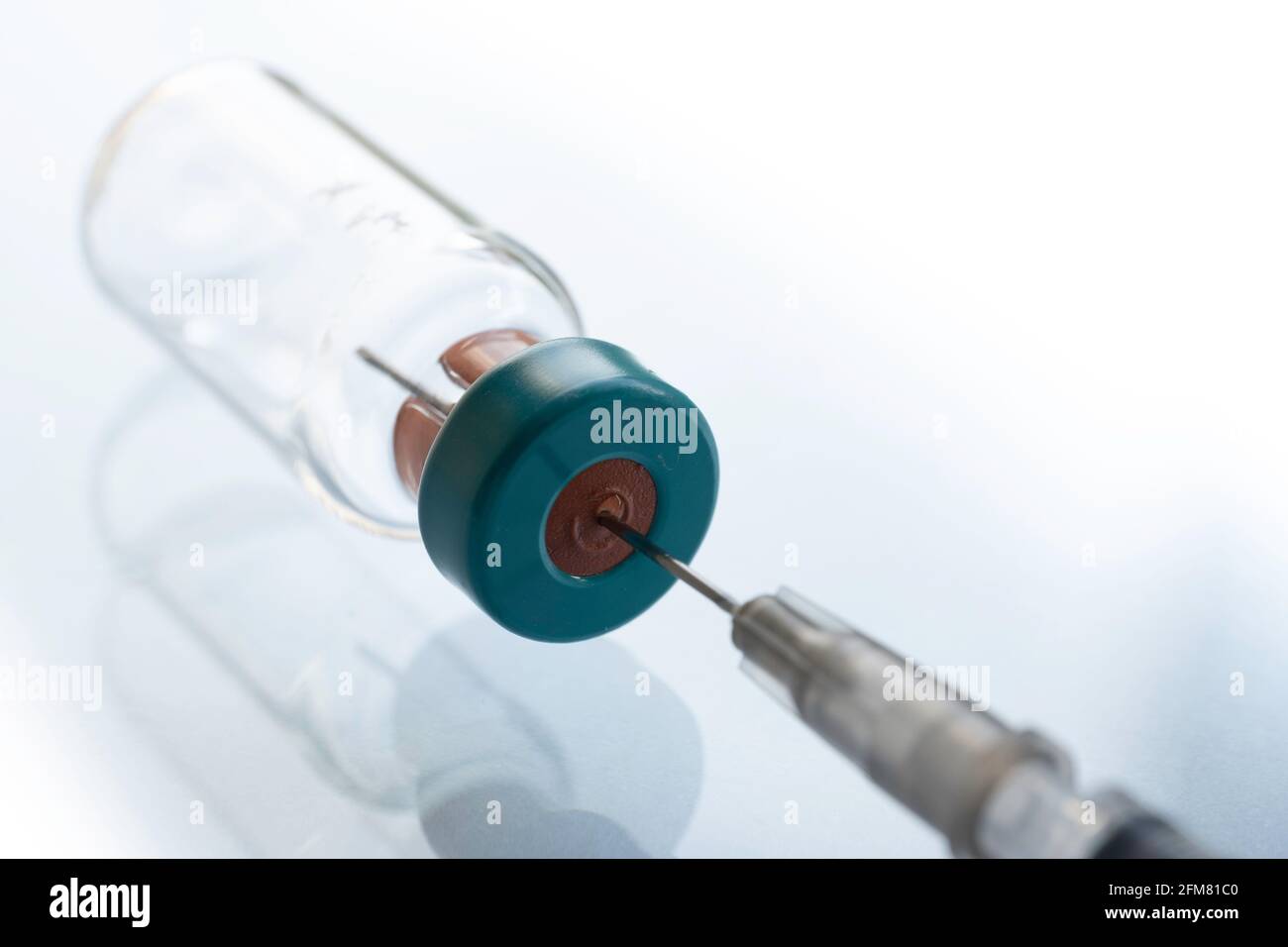 Syringe needle protrudes through the rubber cap of a vaccine bottle