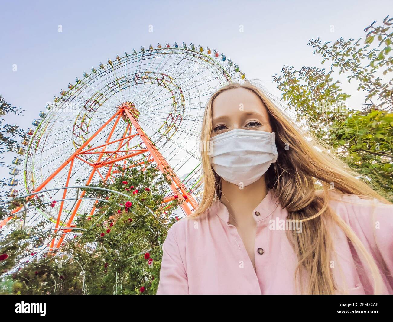 A woman in a pink dress takes a selfie on the background of a ferris wheel Stock Photo