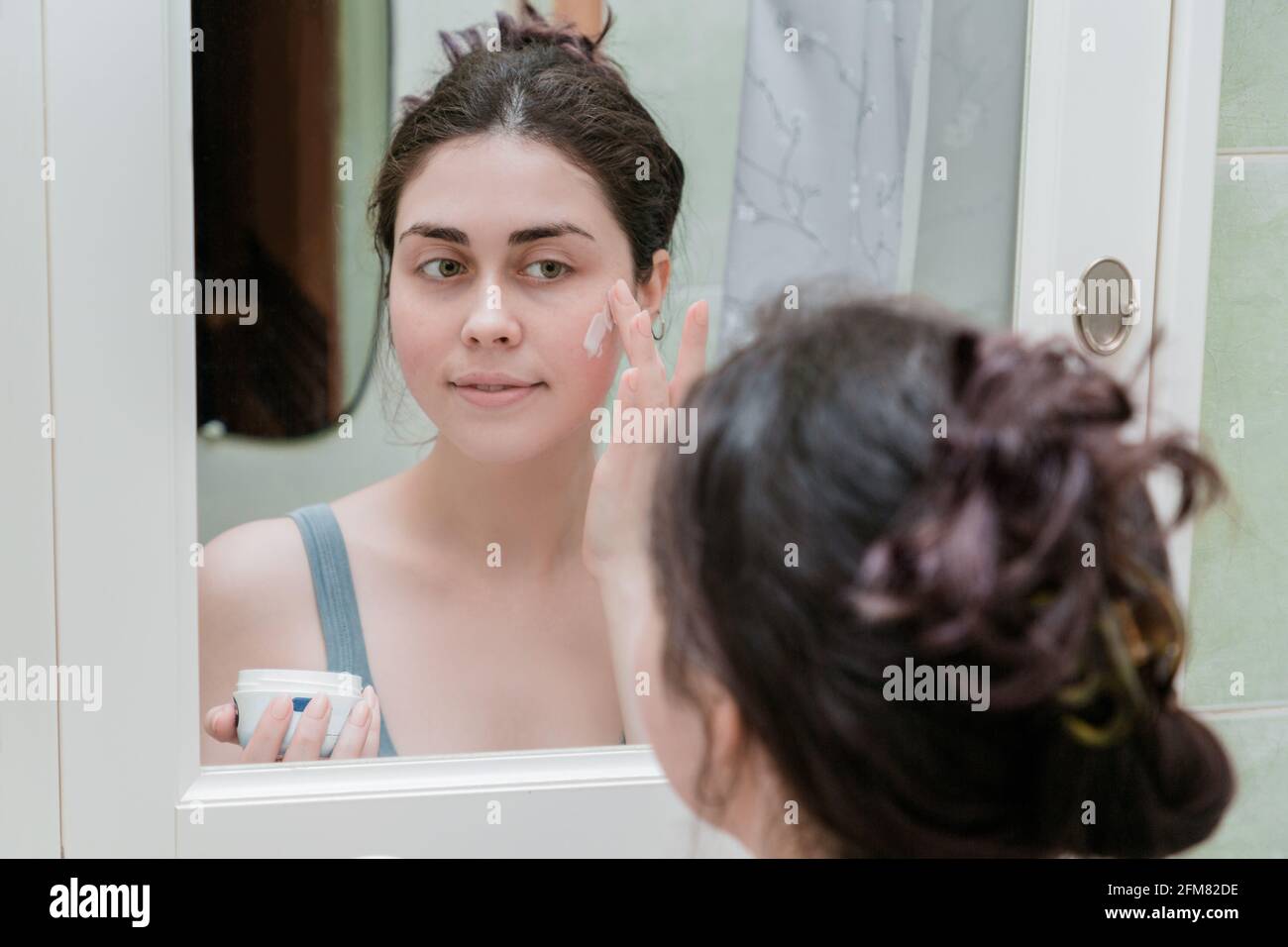Young beautiful teenage girl touching her face before the mirror and ...