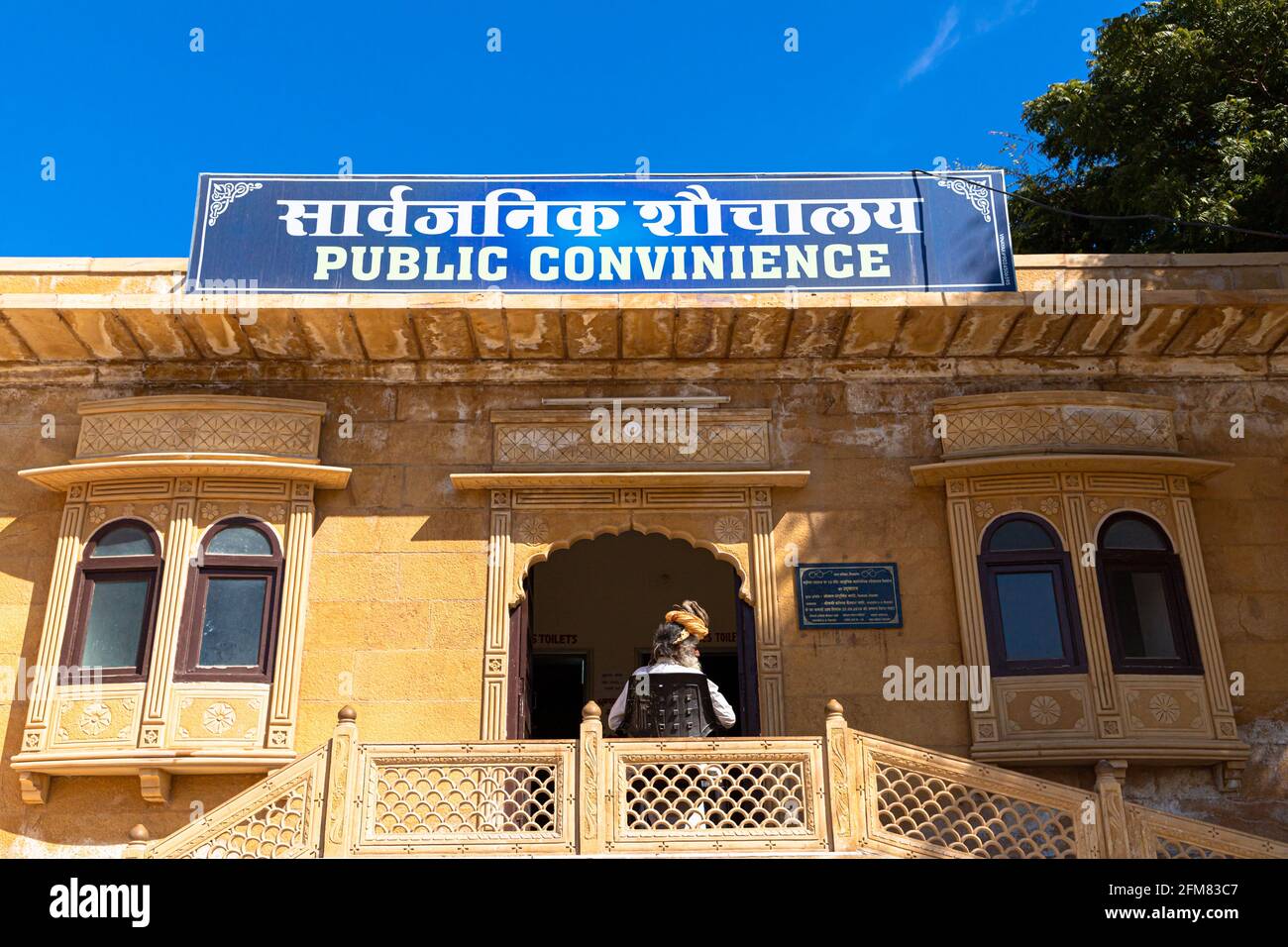 a aged man sitting in front of public toilet at jaisalmer. Stock Photo