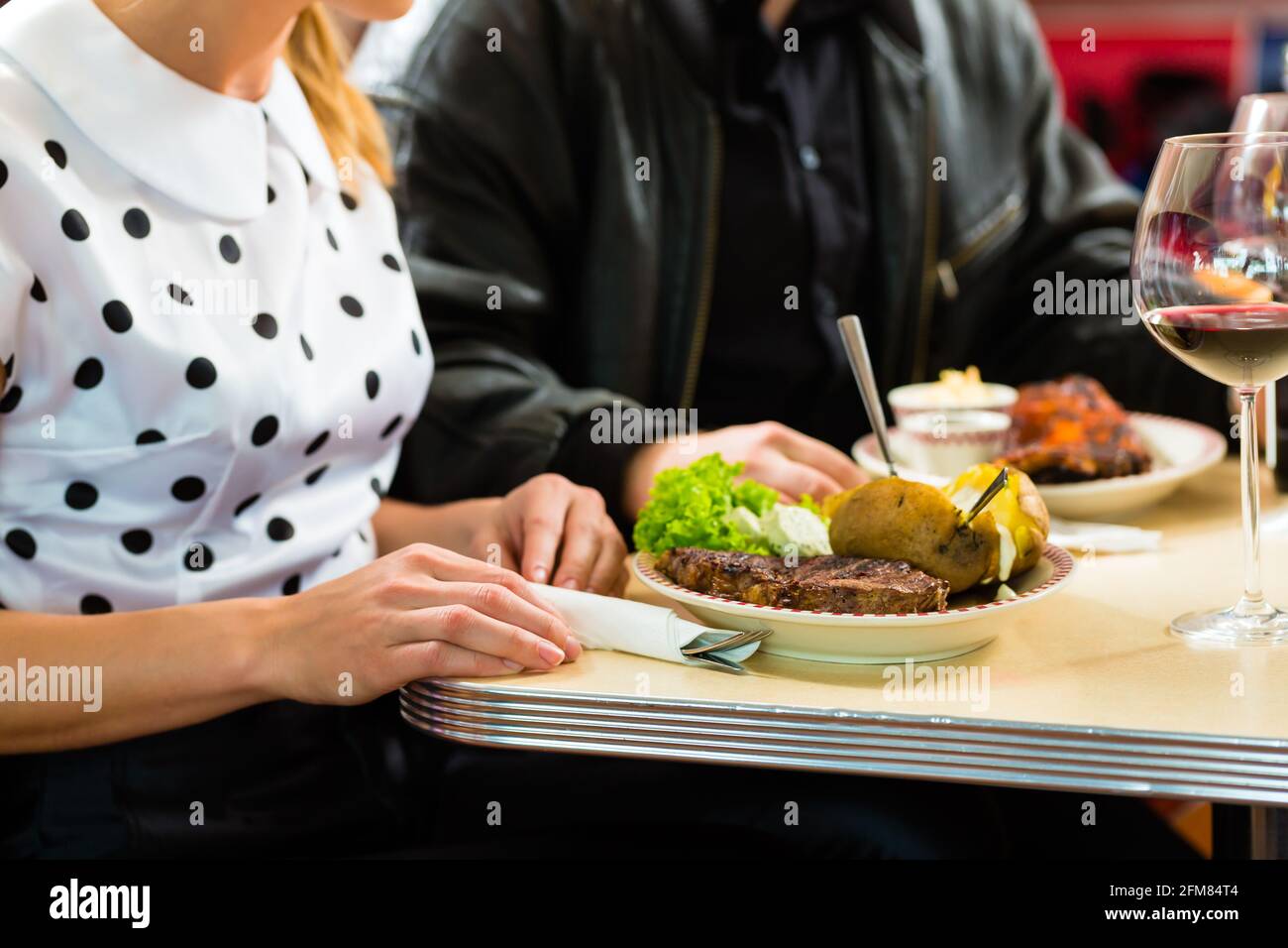 Young couple eating fast food and drinking red wine in a American retro