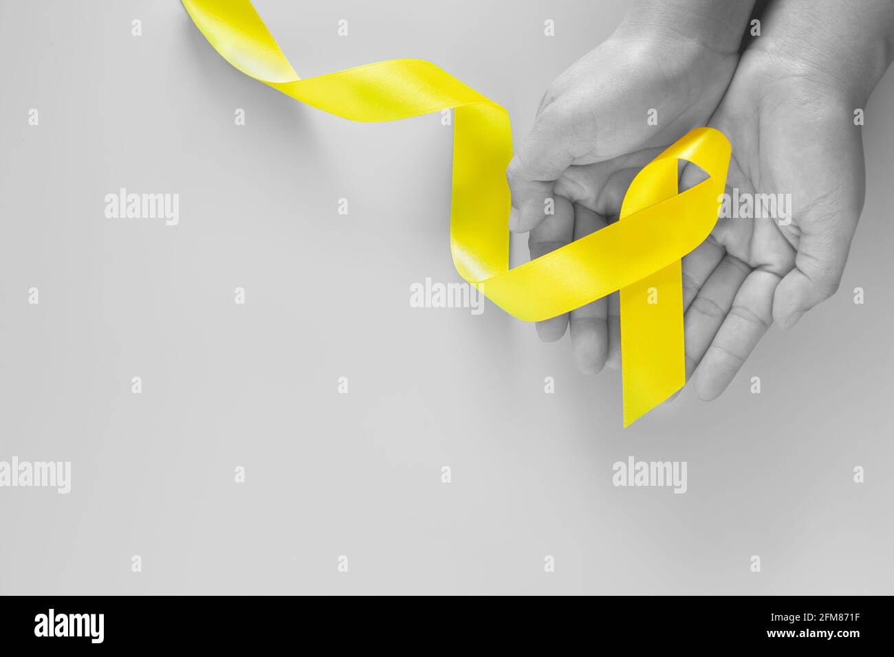 Hand holding Yellow ribbon on green background, copy space. Bone cancer Sarcoma Awareness childhood cancer cholangiocarcinoma gallbladder cancer world Stock Photo