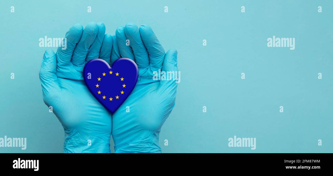Doctors hands wearing surgical gloves holding European Union flag heart Stock Photo