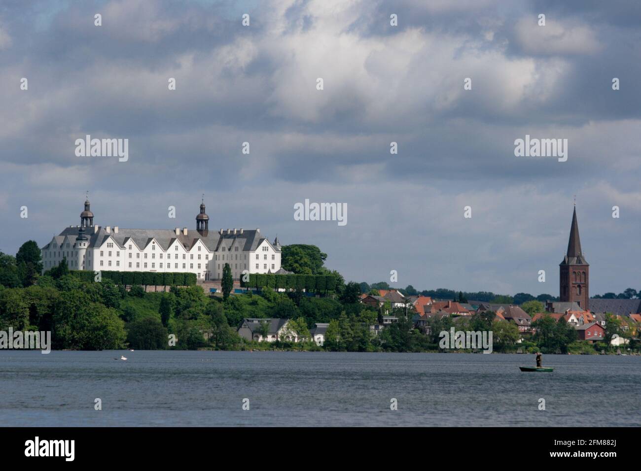 Lakeside view of the beautiful castle and church of Plön, Germany with cloudy sky in the background and sun shining on the landmark Stock Photo