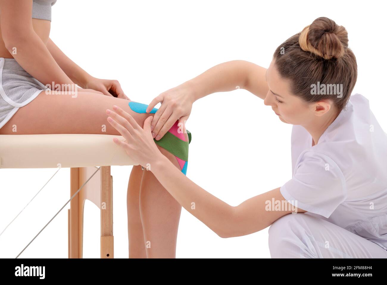 Manual, physio and kinesio therapy techniques performed by female physiotherapist on a training plastic spine and a female patient isolated on white b Stock Photo