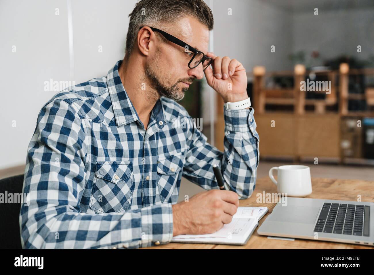 Focused grey man writing down notes while working with laptop in office Stock Photo