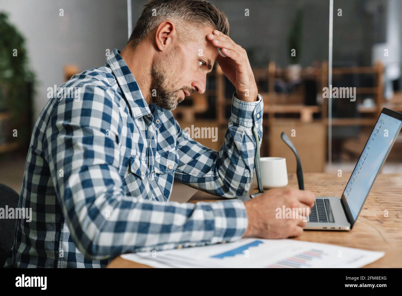 Brooding grey man working with laptop while sitting in office Stock Photo