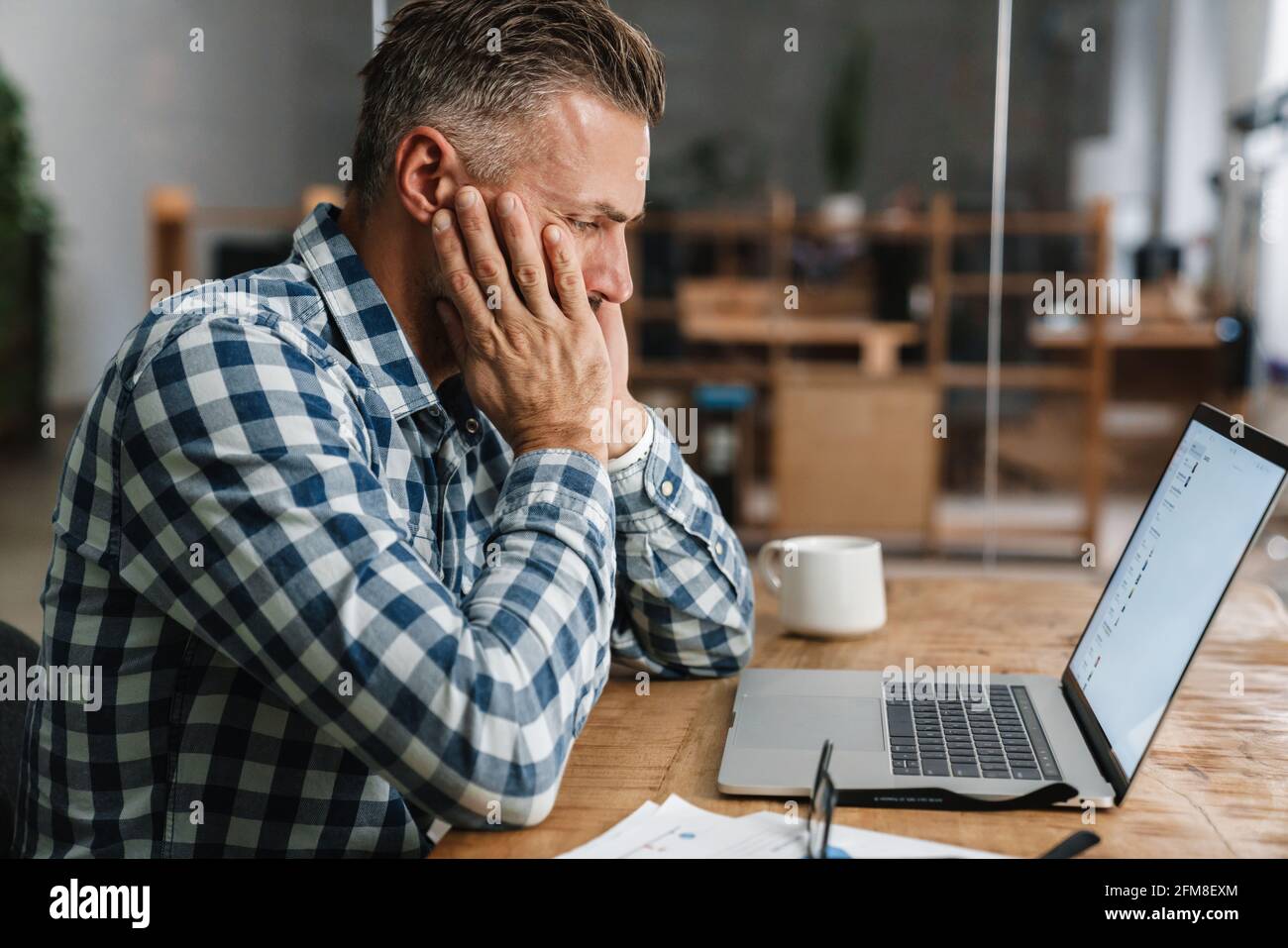 Tired grey man working with laptop while sitting in office Stock Photo