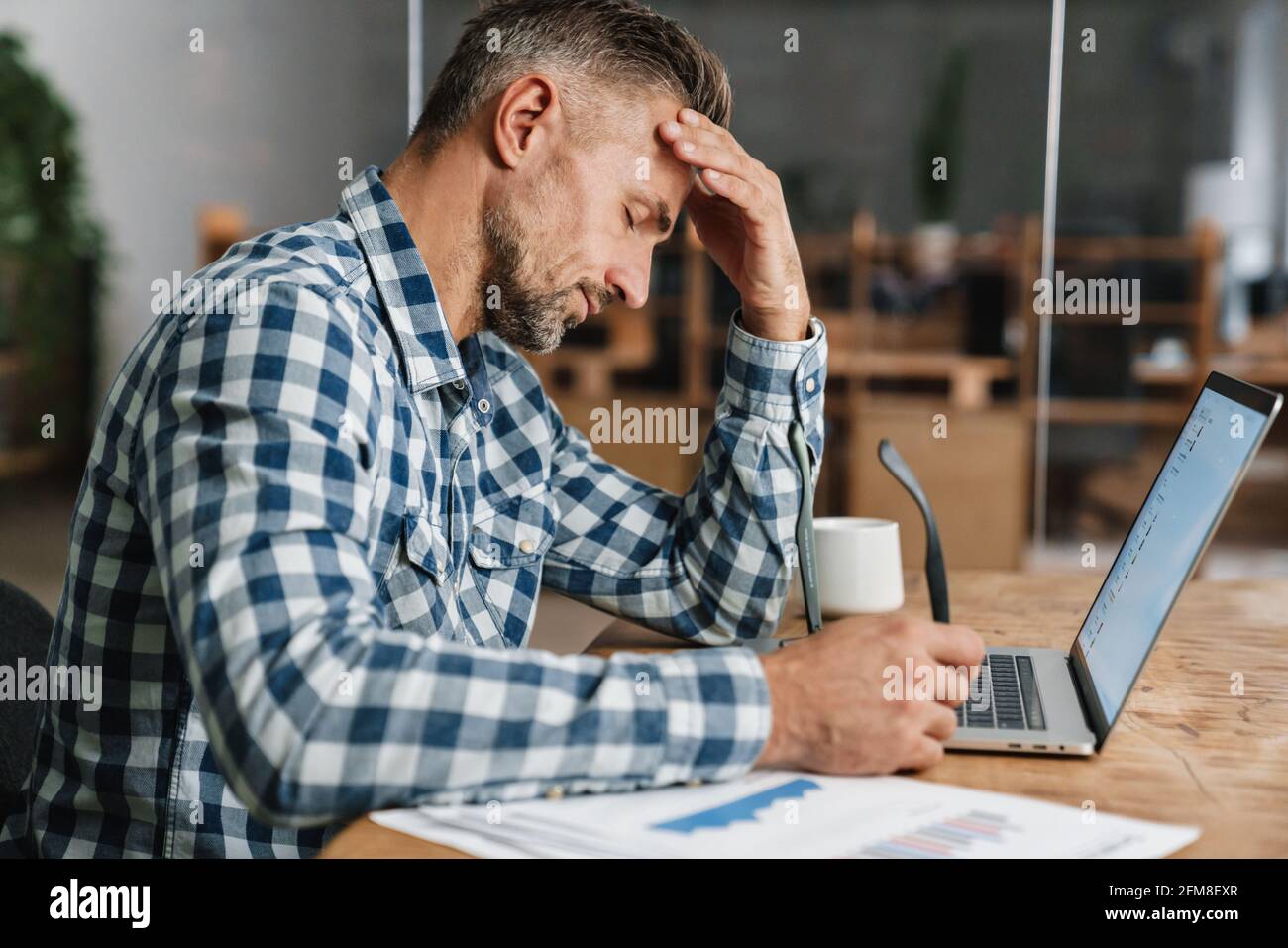Tired grey man working with laptop while sitting in office Stock Photo