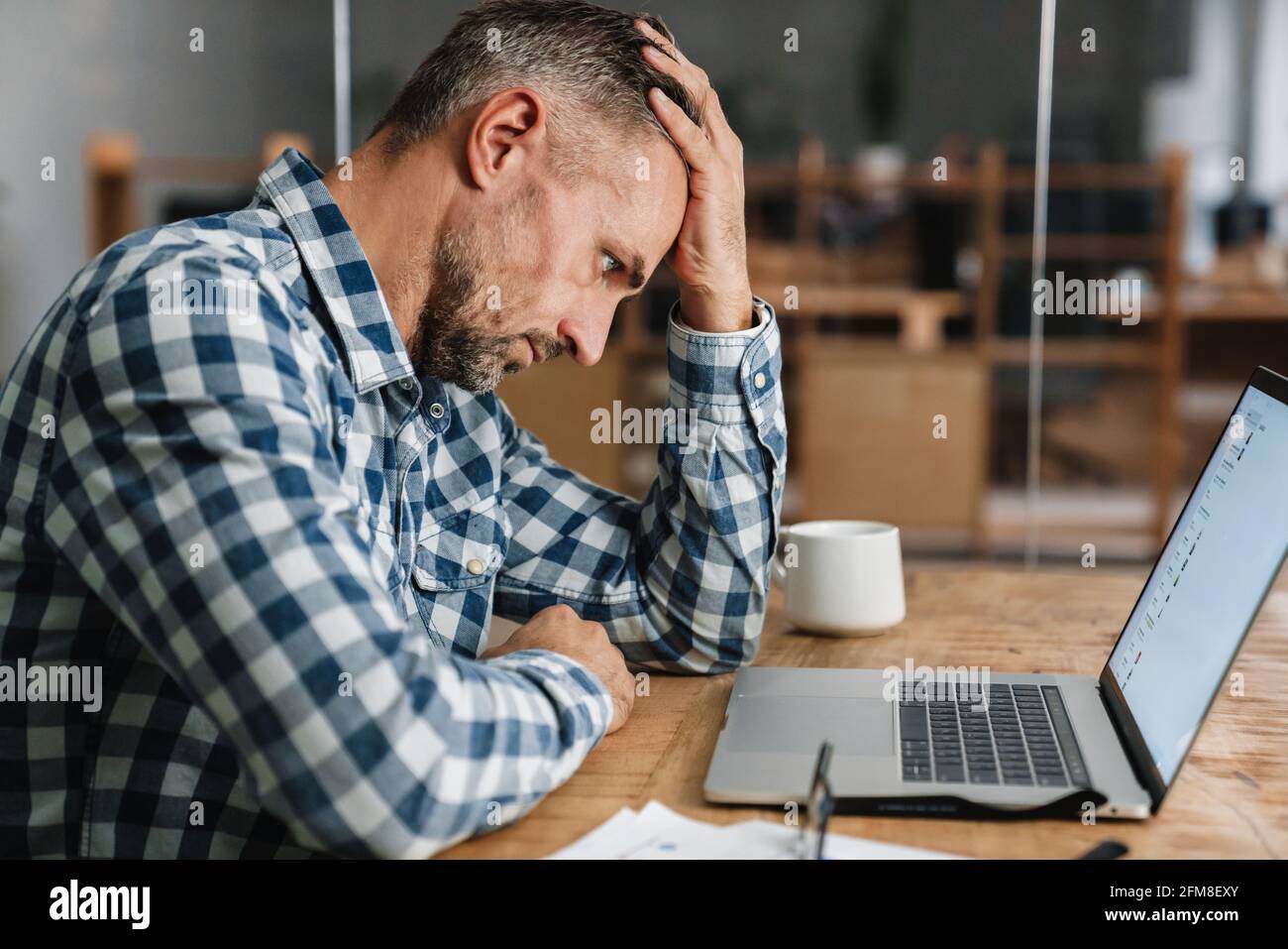 Tired grey man working with laptop while sitting in office Stock Photo