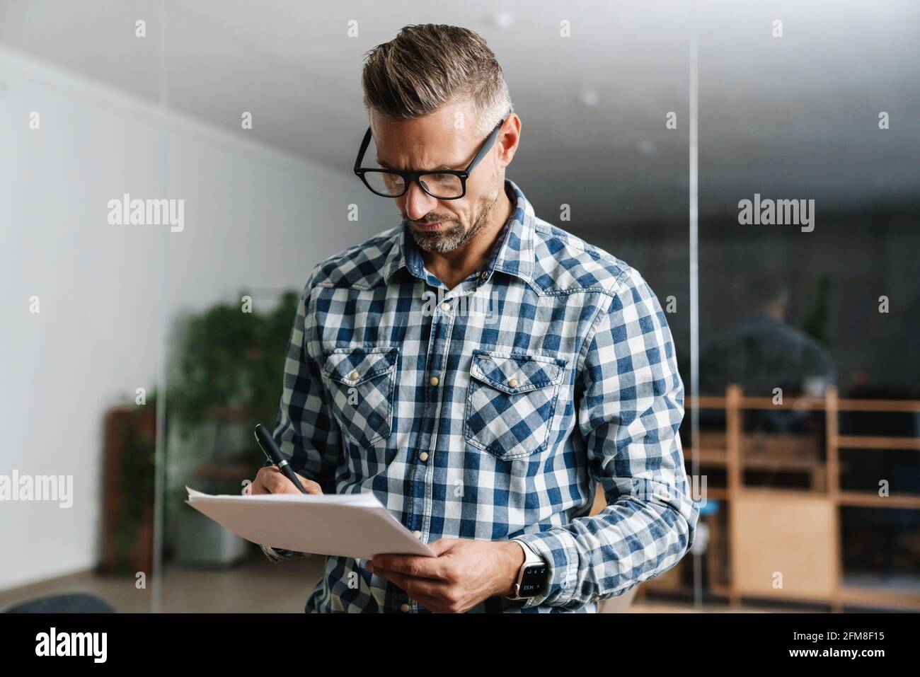 Serious white-haired man working with papers while standing in office Stock Photo