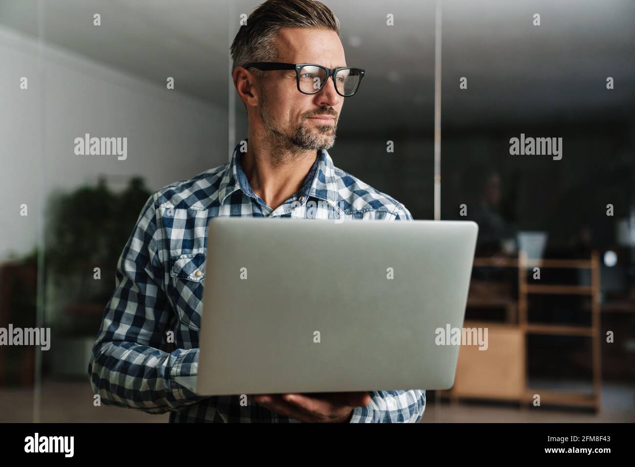 Serious white-haired man working with laptop while standing in office Stock Photo