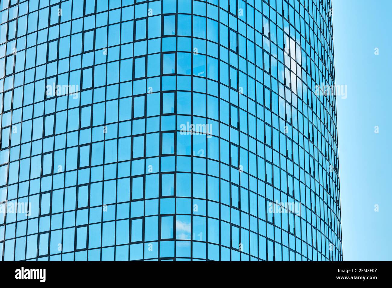 Stylish highrise office building with shiny blue glass facade reflecting bright sunlight against clear blue sky on sunny day Stock Photo