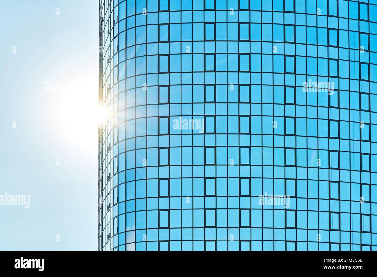 Stylish highrise office building with shiny blue glass facade reflecting bright sunlight against clear blue sky on sunny day Stock Photo