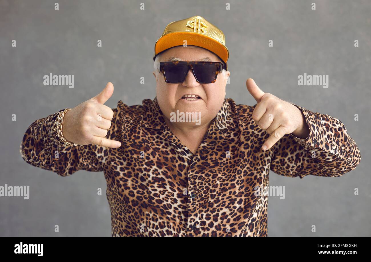 Funny rich senior man in baseball cap, glasses and leopard shirt enjoying music and having fun Stock Photo