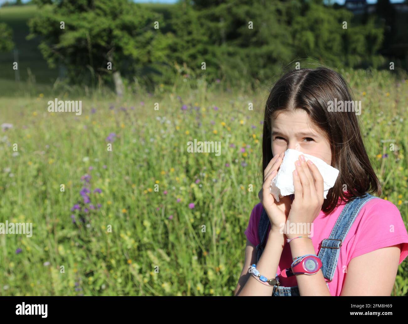 young girl allergic to pollen while blowing her nose in the middle of the meadow in spring Stock Photo
