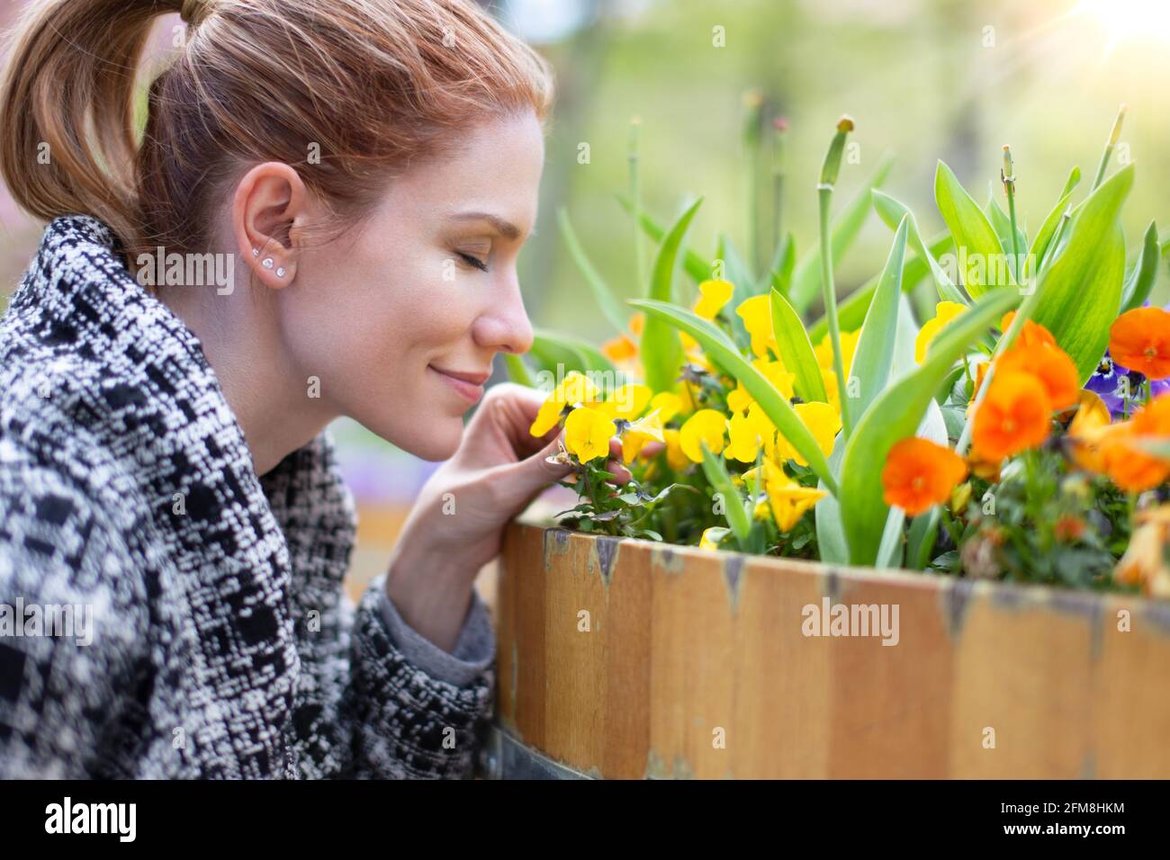 Young Casucasian woman smelling flowers at spring in public park, profile view, outdoors Stock Photo