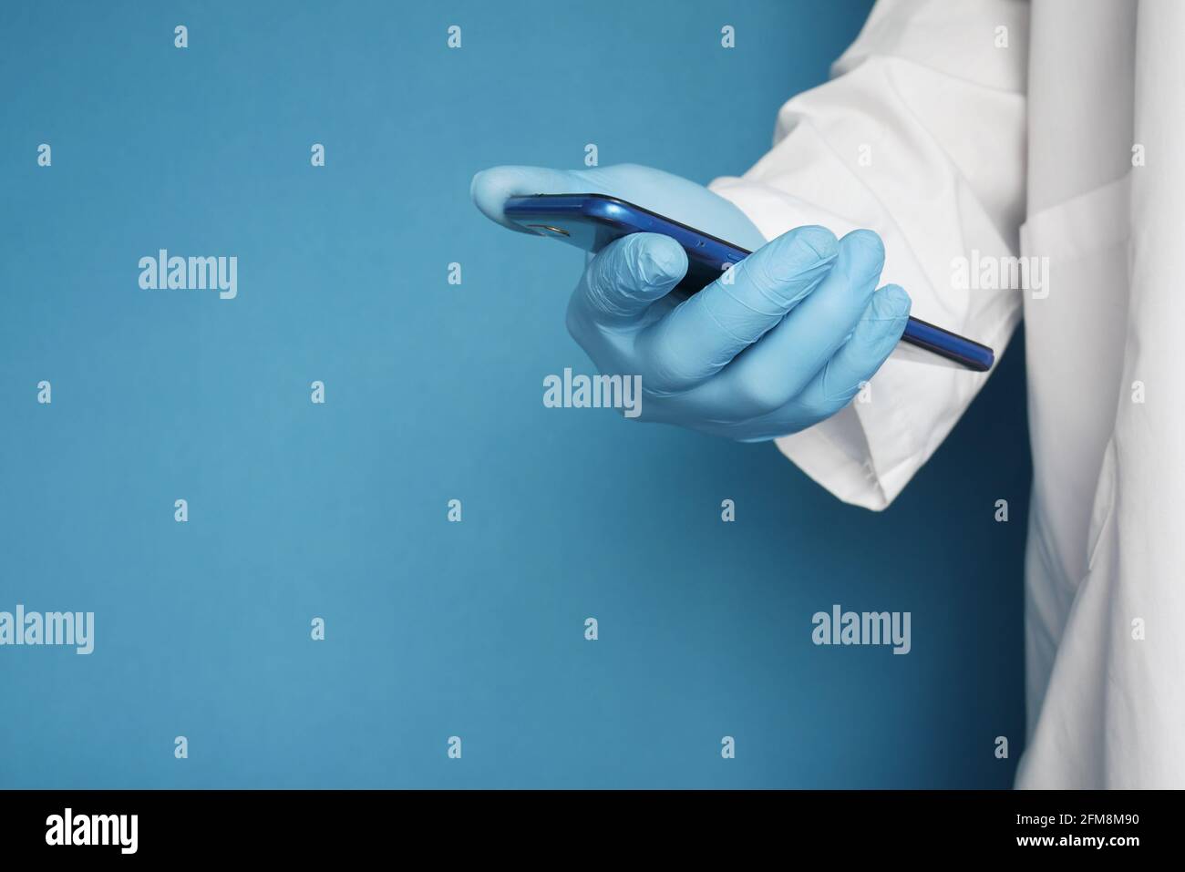 doctor's hand in protective gloves using a smartphone against blue background Stock Photo