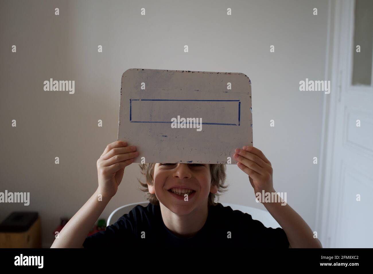 Primary school age child being schooled at home - maths, holding up drawing on whiteboard of a rectangle. Stock Photo