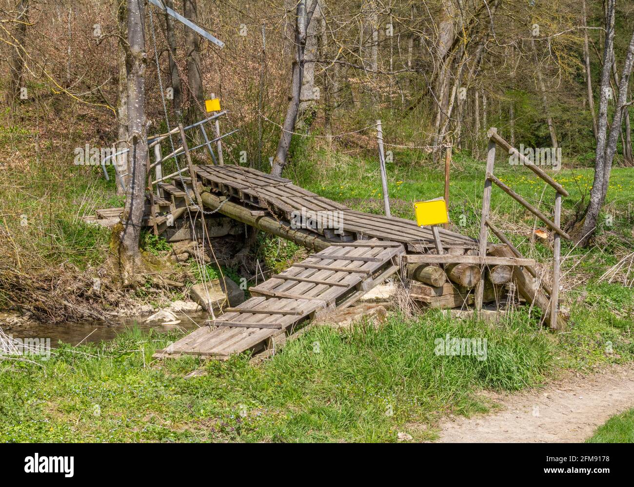 Improvised ramshackle wooden self-made bridge over a rivulet in sunny ambiance Stock Photo