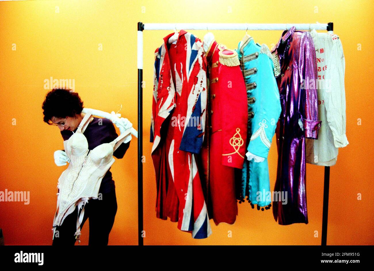 EXHIBITION OF ROCK AND ROLL COSTUMES AT THE BARBICAN.LISA COLLINS OF THE BARBICAN TRIES MADONNA'S JEAN-PAUL GAULTIER BUSTIER. BEHIND HER ON THE RACK IS L-R: DAVID BOWIE'S UNION JACK FROCK COAT; GEORGE HARRISONS RED COAT FROM SGT. PEPPER; PAUL MCCARTNEY'S BLUE COAT FROM SGT. PEPPER; AND PRINCE'S PURPLE ROBE. Stock Photo