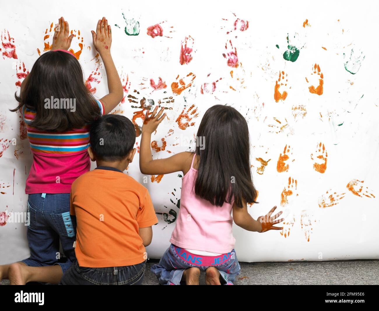 YOUNG CHILDREN PAINTING ON WHITE PAPER WITH THEIR HAND TO CREATE