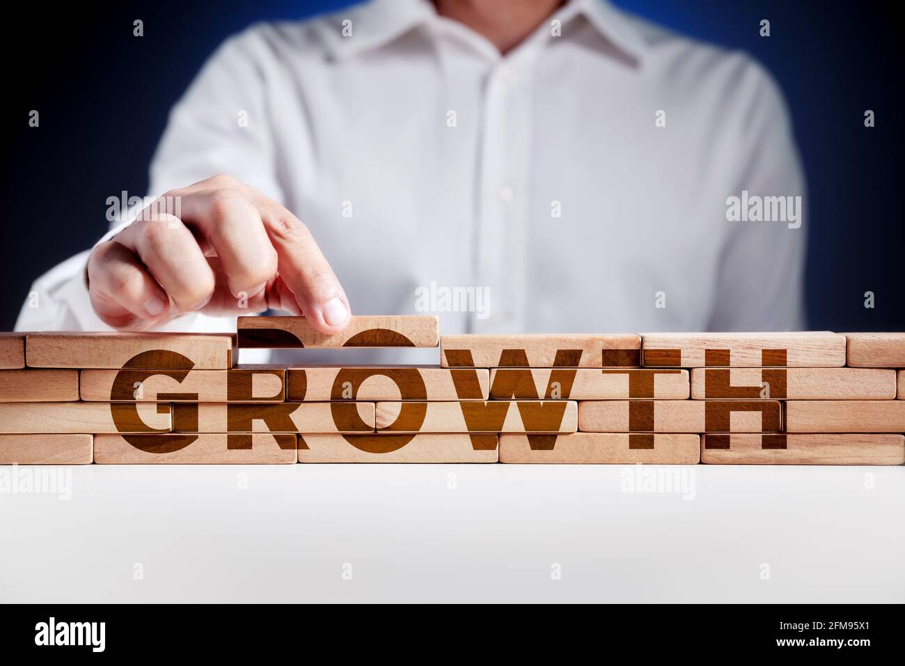Businessman builds a structure of wooden blocks with the word growth. Business or career growth concept. Stock Photo