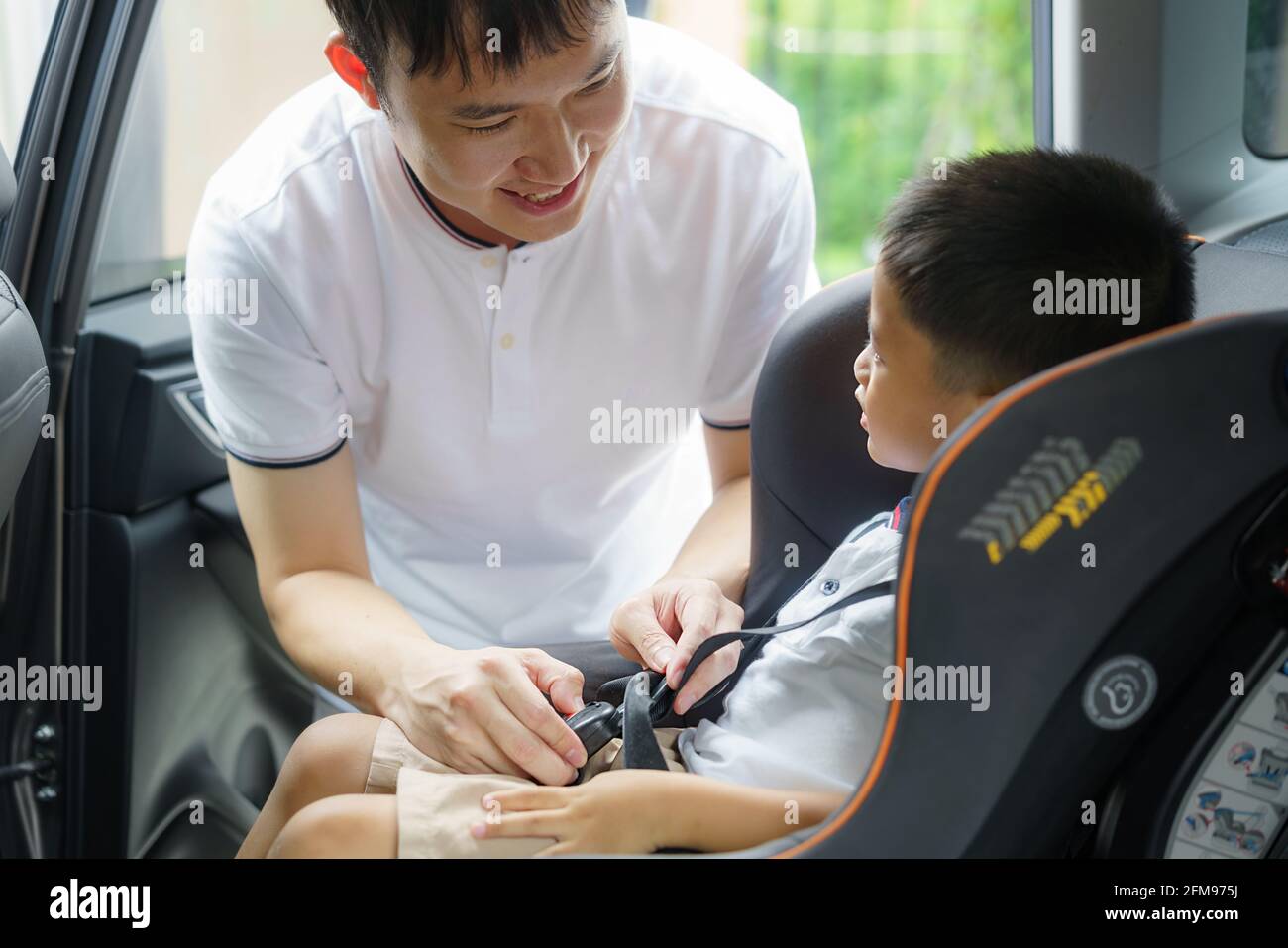 Asian father clicking child into car seat while traveling, fathers interact with their children throughout the day. Stock Photo