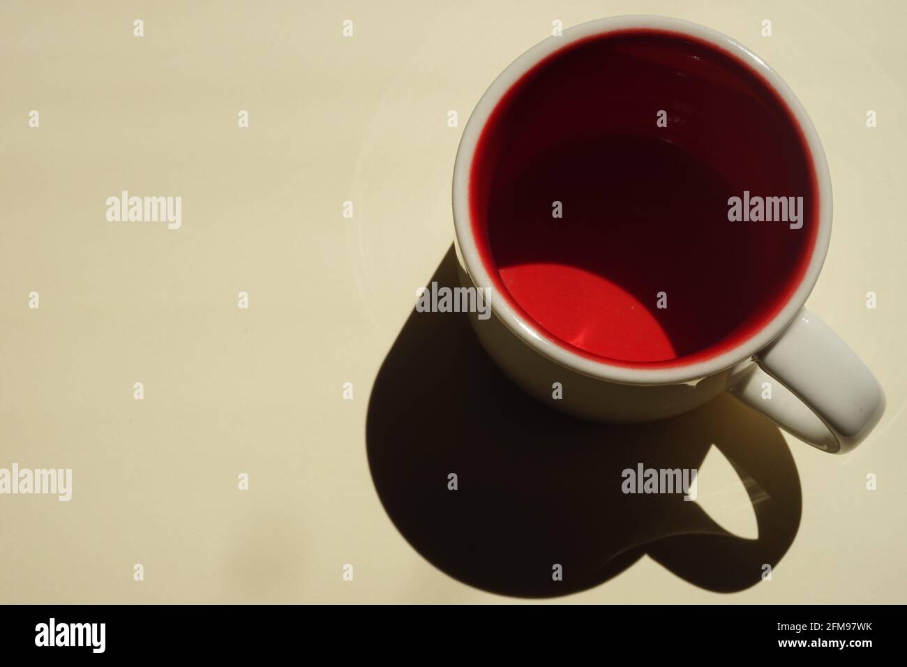 Beige cup with red inside on a beige table. Light and shadow. Top view. Stock Photo